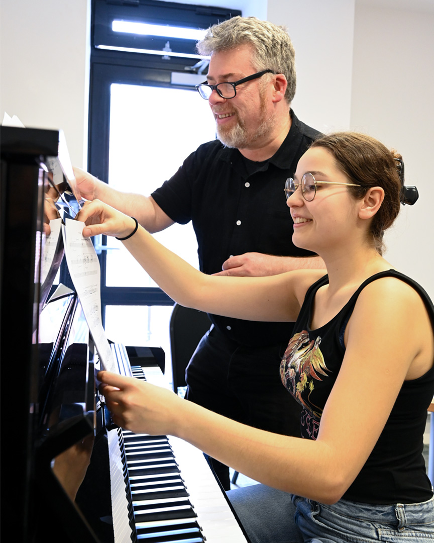 A professor and student looking at music sheets on a piano.